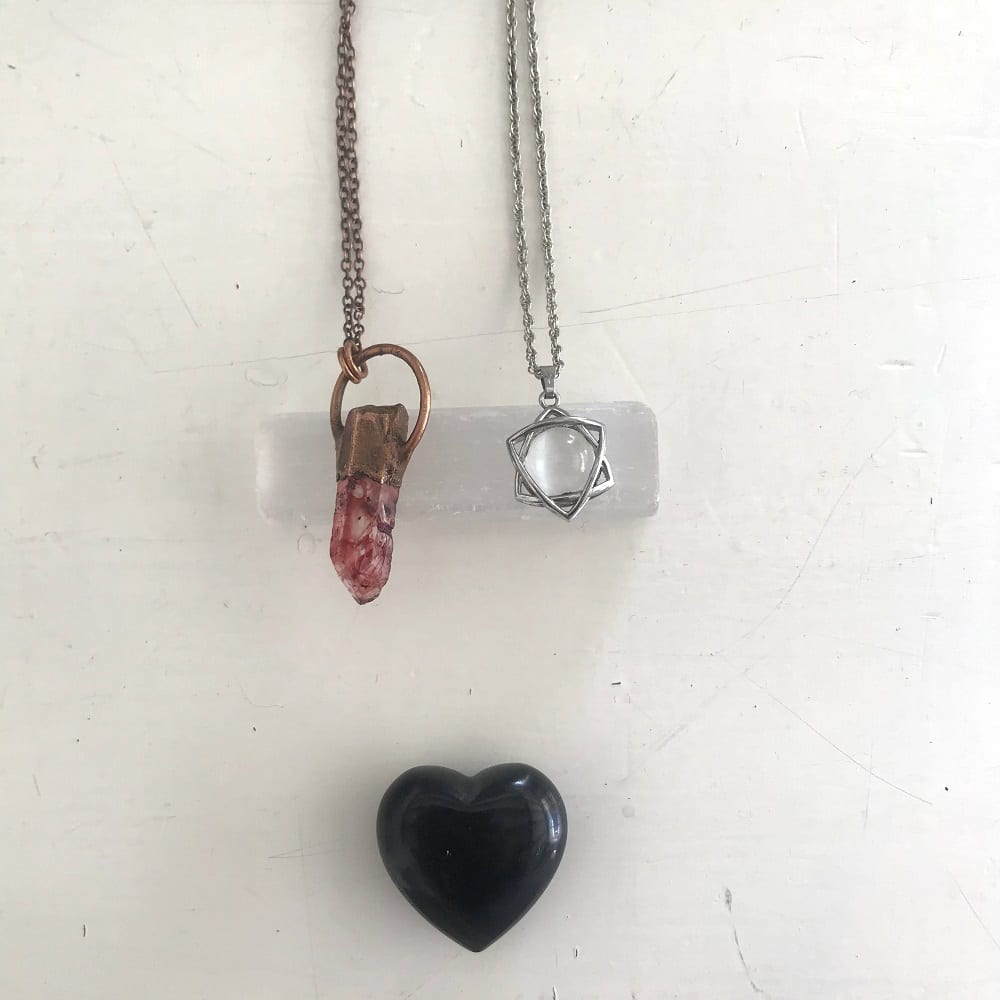two pendulum necklaces next to black heart crystal